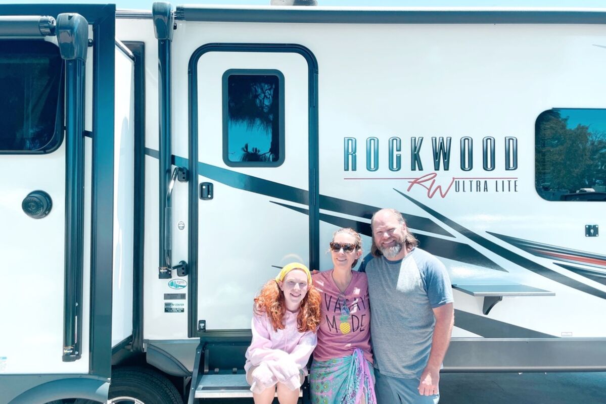 A%20family%20of%203%20standing%20in%20front%20of%20an%20RV%20that%20says%20Rockwood%20on%20it%2E