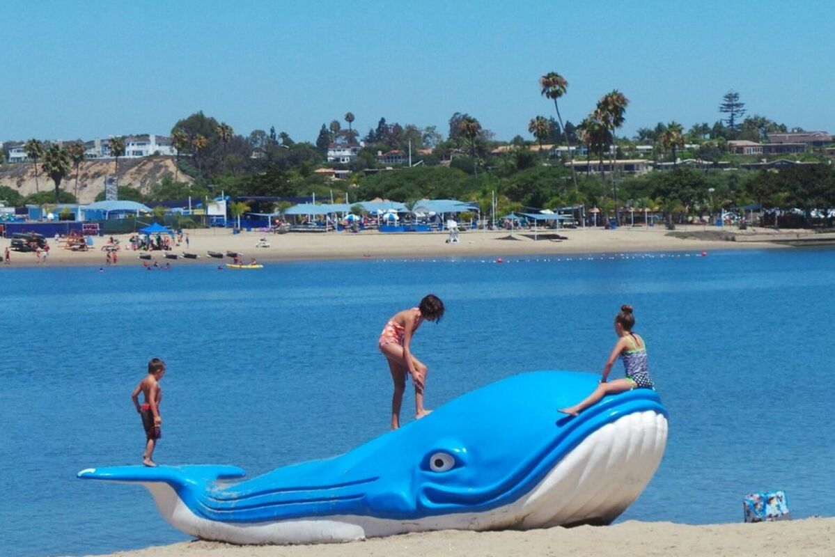 A%20giant%20blue%20floatable%20plastic%20whale%20on%20a%20beach%20with%20kids%20playing%2E
