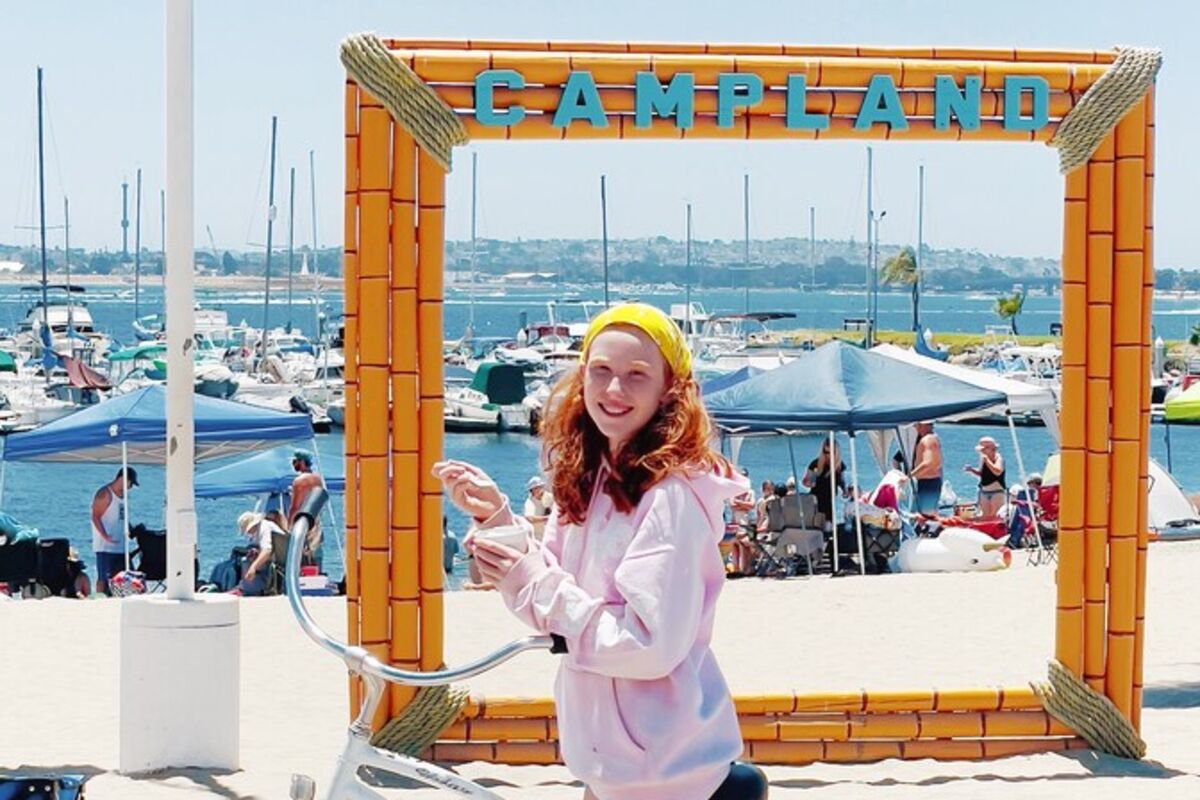 Girl%20on%20bike%20eating%20ice%20cream%20at%20the%20beach%20with%20a%20Campland%20sign%2E